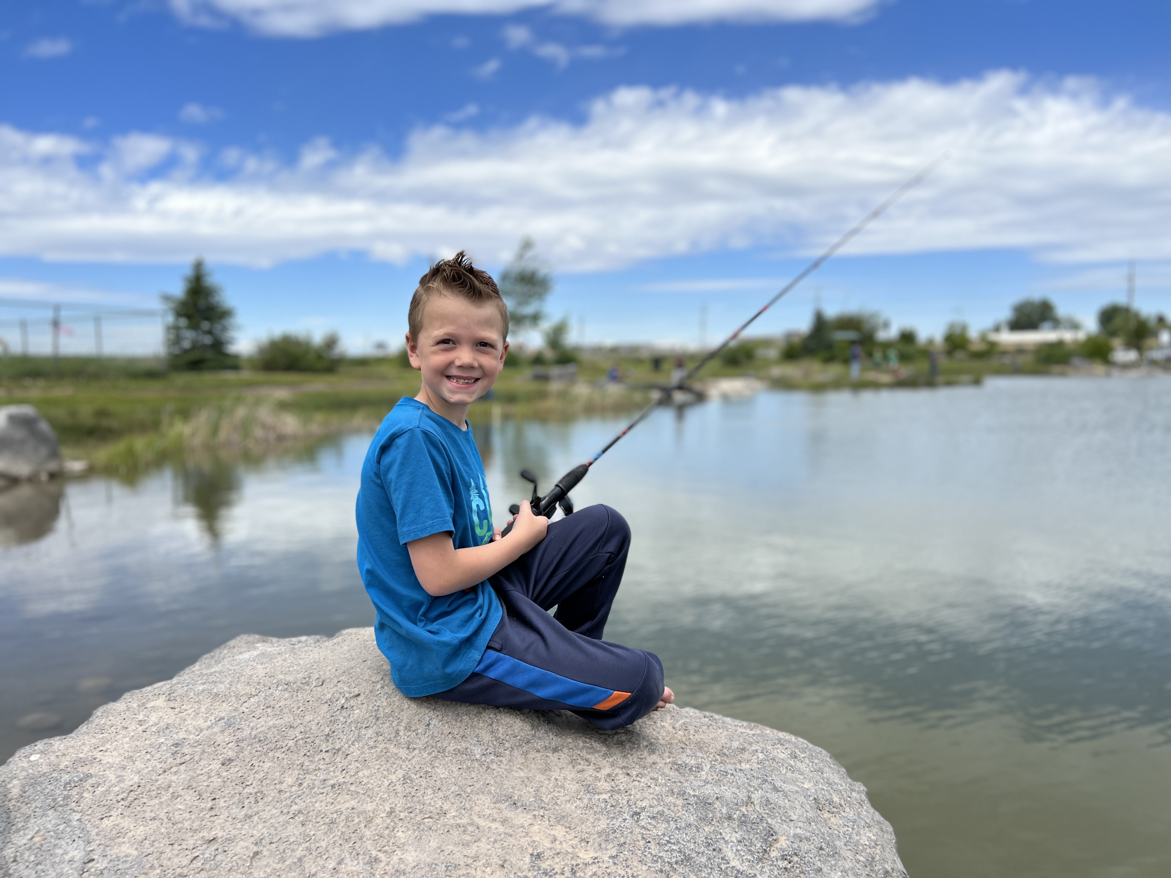Young Boy sitting on a rock, smiling while fishing a local pond