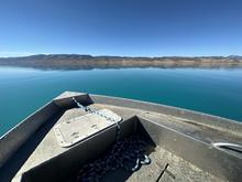 The front of a boat shown atop the bright blue waters of Bear Lake.  Foothills are in the background under a blue sky.